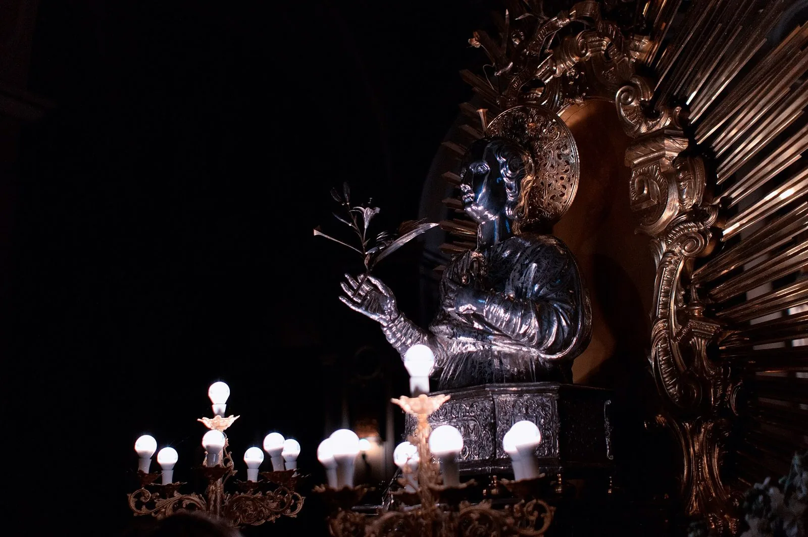 Il busto d'argento di San Potito con la palma del martirio, illuminato da candelabri davanti a una raggiera dorata