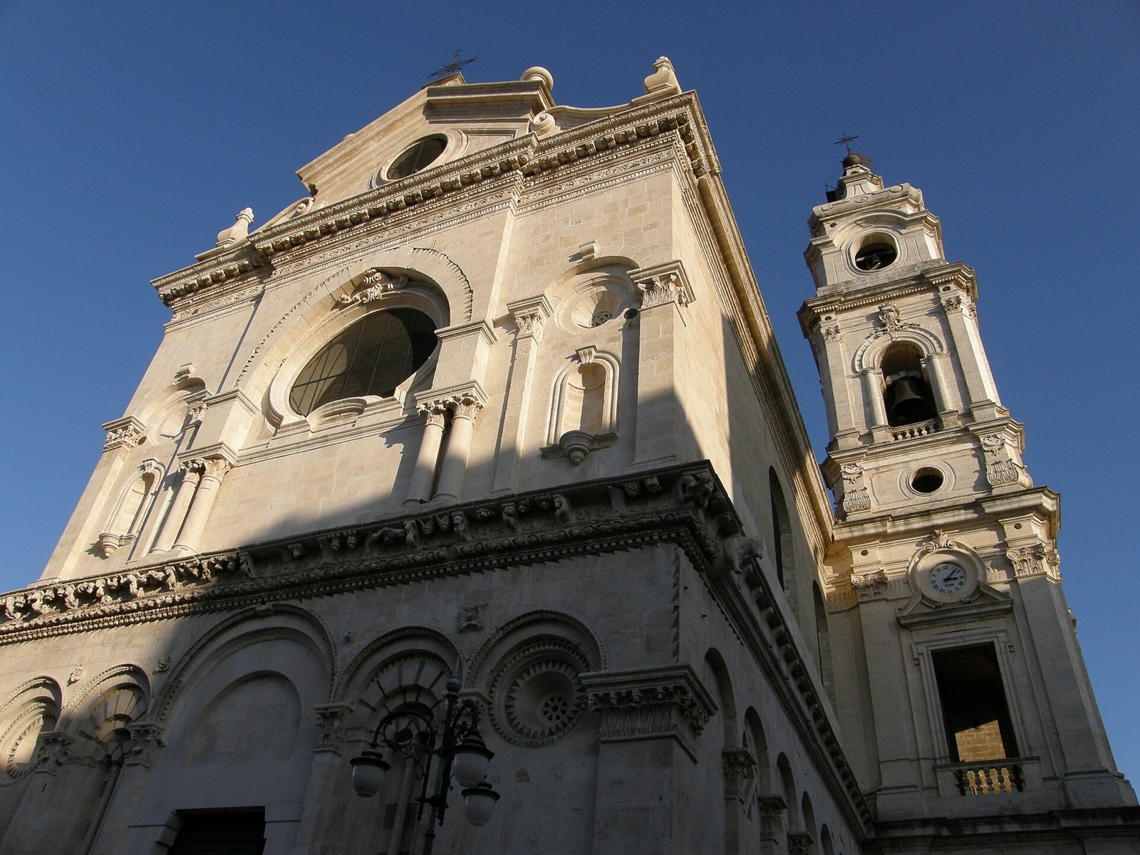 Facciata della cattedrale di Foggia vista dal basso, con la parte inferiore romanica ad archi, la parte superiore barocca e il campanile