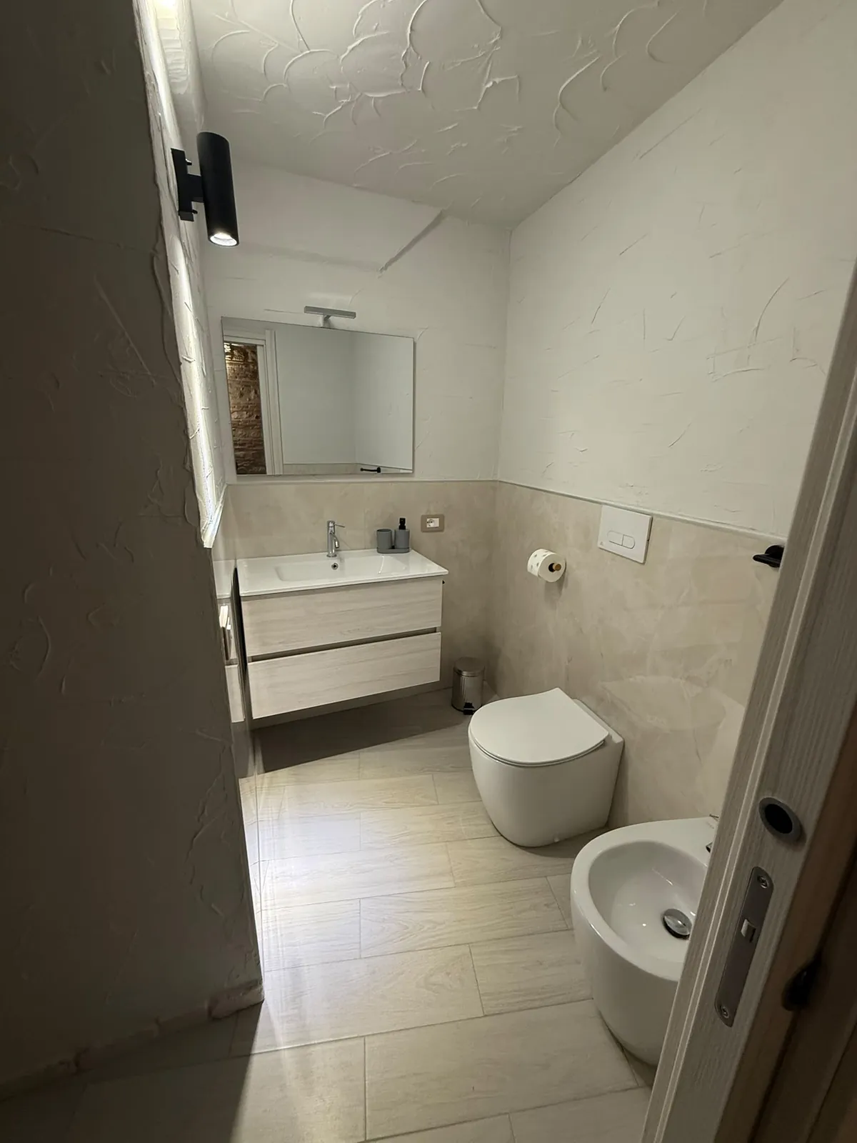 Il bagno con il lavabo sospeso, i sanitari e la parete in pietra